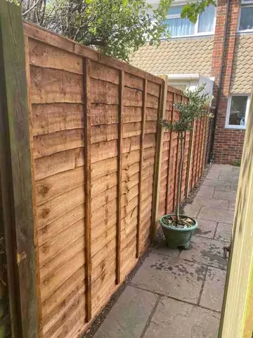 A run of new brown lap fence panels along a garden path