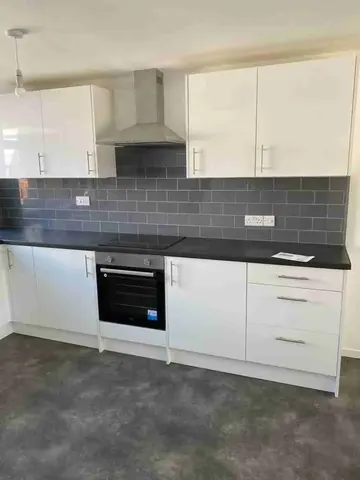 A row of white gloss kitchen units with a black worktop, grey metro tiles, built-in oven and cooker hood